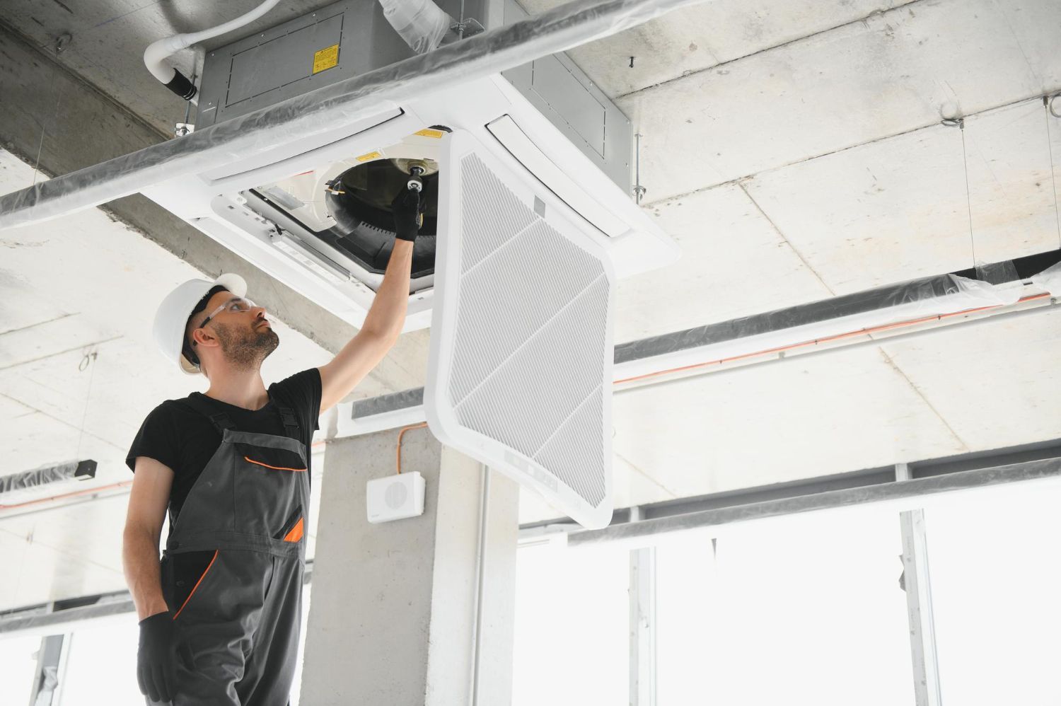 Technician working on a ceiling-mounted HVAC unit in a bright unfinished room