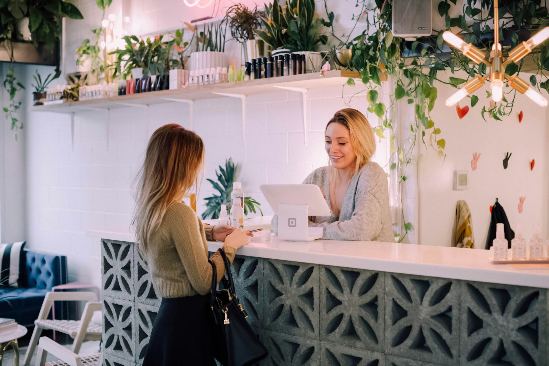 Customer speaking with barista at a modern café counter, with hanging plants and warm lighting.