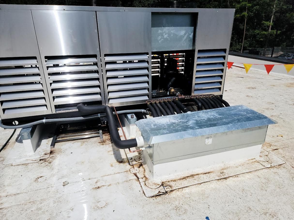 Industrial rooftop HVAC units with vents and ducting beside a solar water heater tank