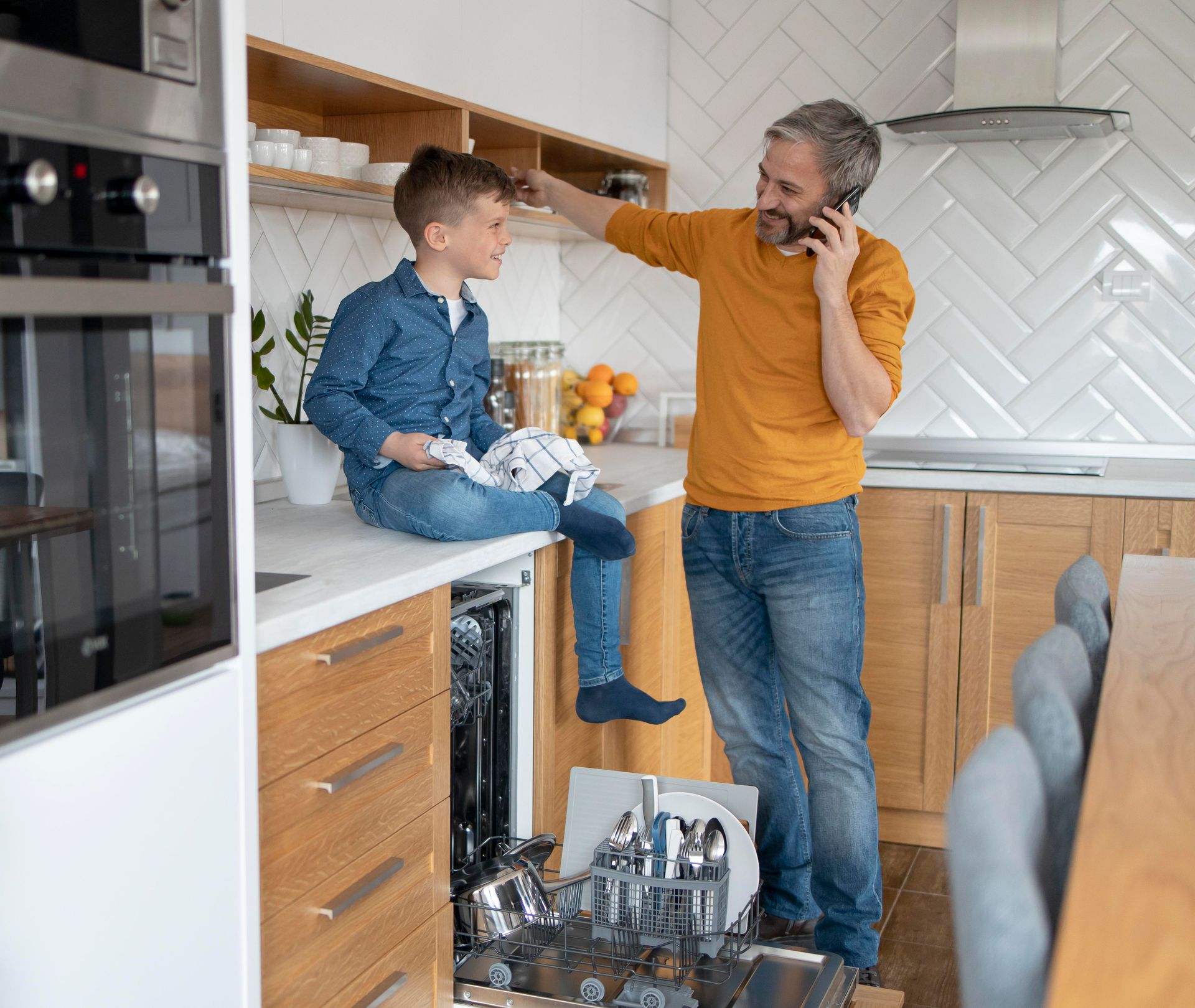 Child and adult talking in a bright kitchen, with the child sitting on the counter and holding fruit.