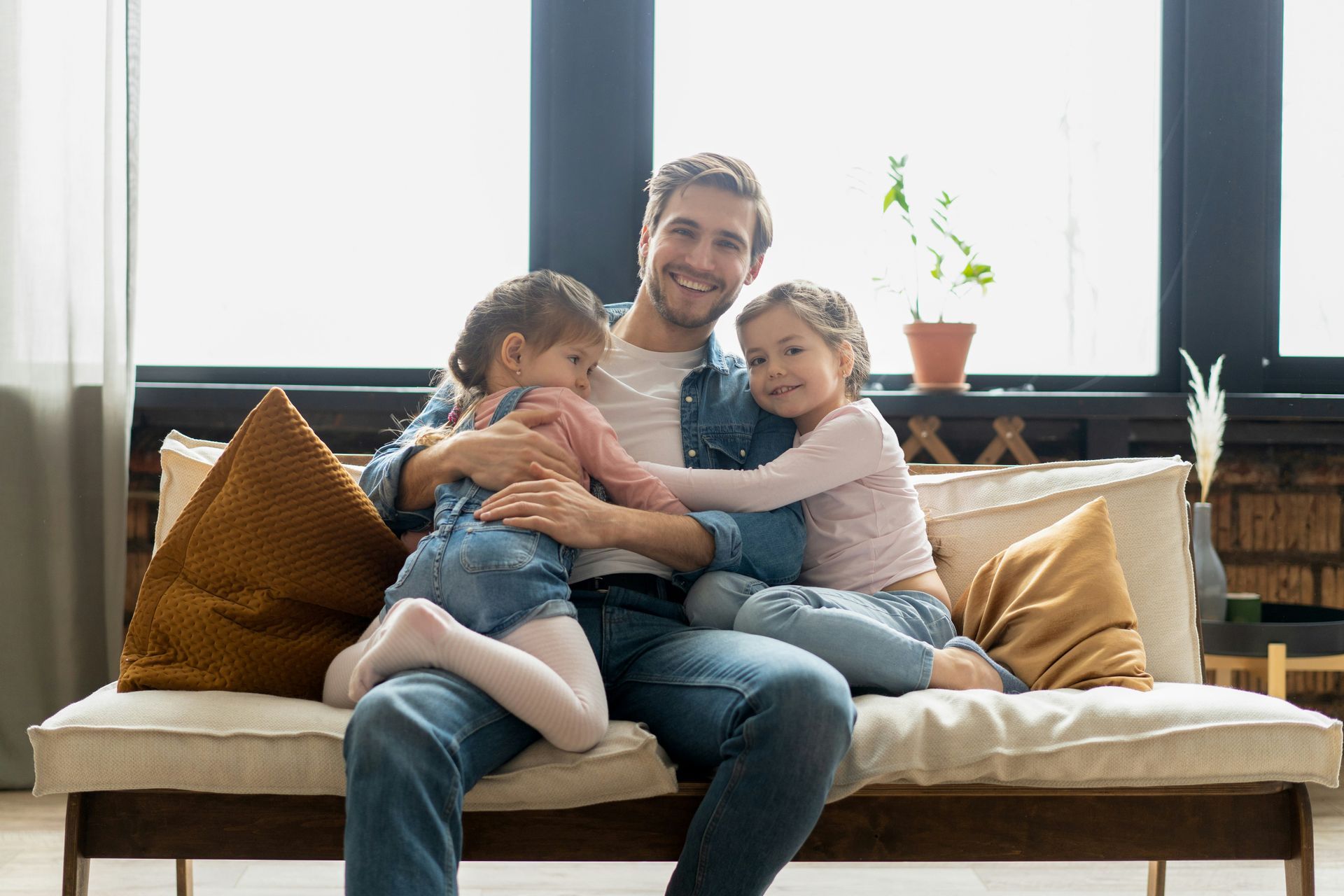 Man sitting on a sofa hugging two smiling children in a bright living room