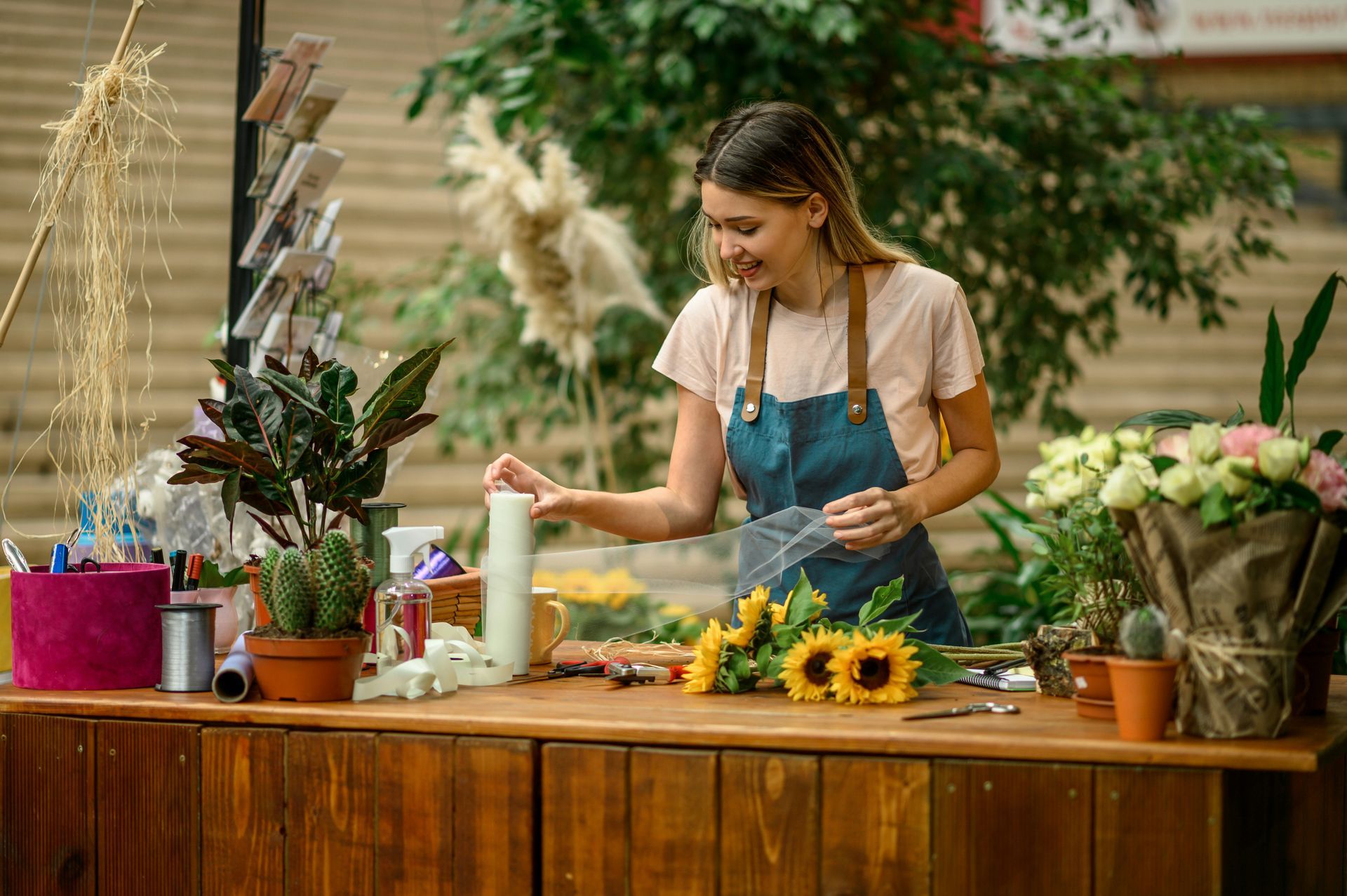 Woman arranging flowers at a market stall with sunflowers and potted plants