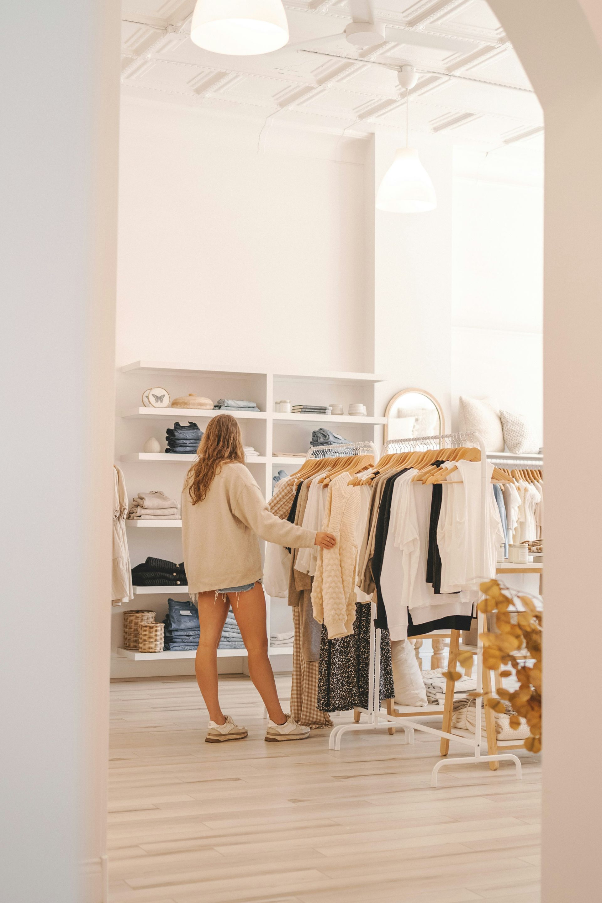 Person browsing clothes in a bright boutique with white shelves and light wood floors
