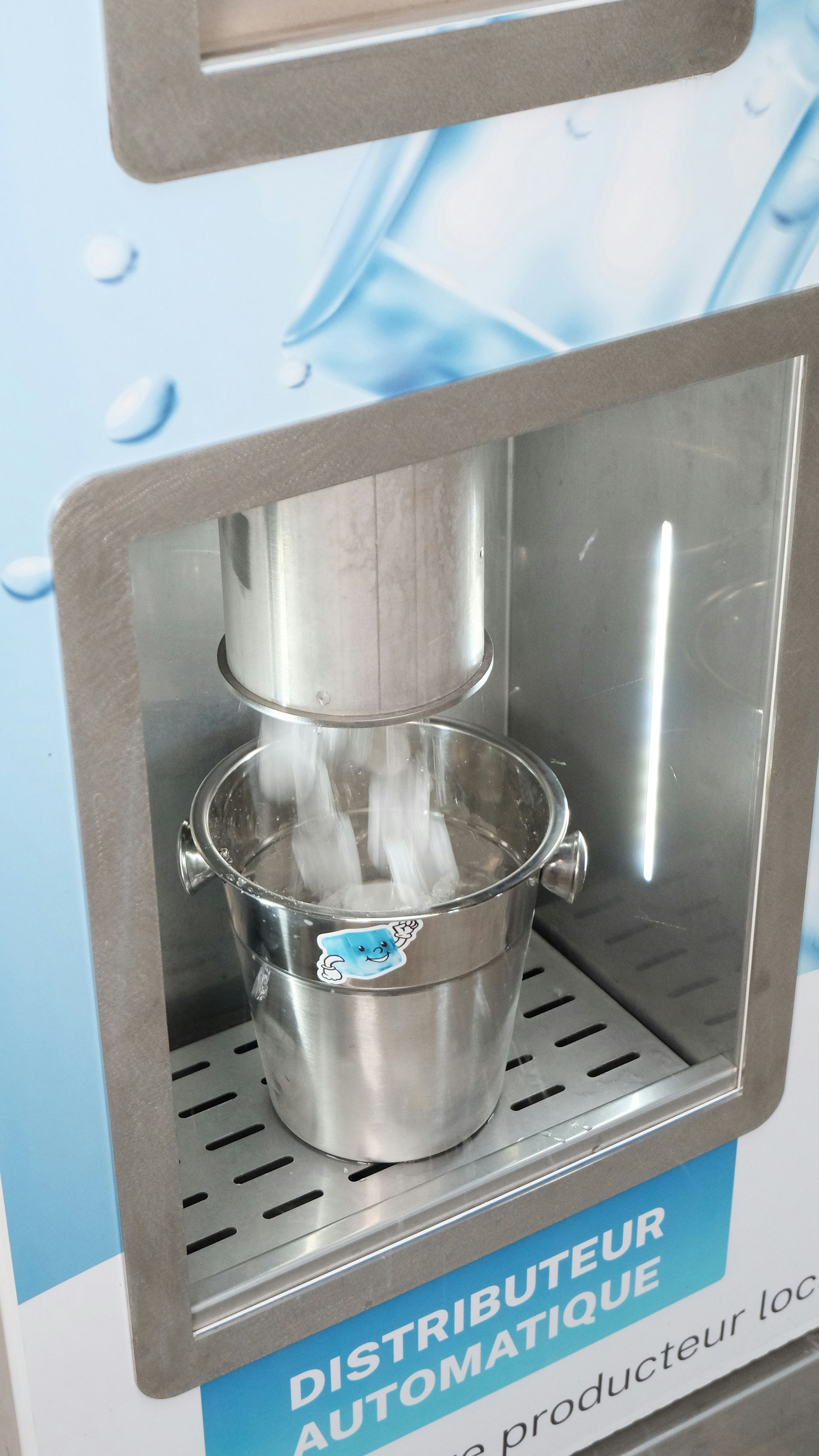 Automatic beverage dispenser filling a metal cup with water behind a glass panel.