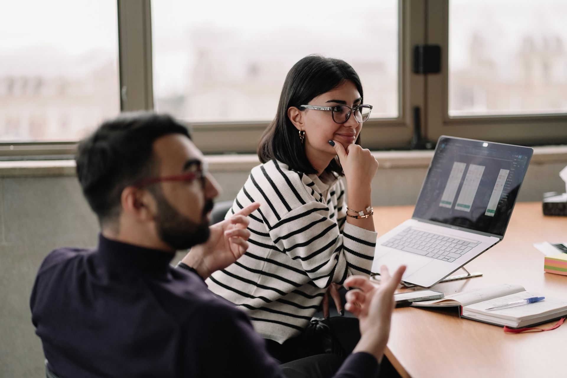 Two coworkers discussing a laptop at a desk in a bright office