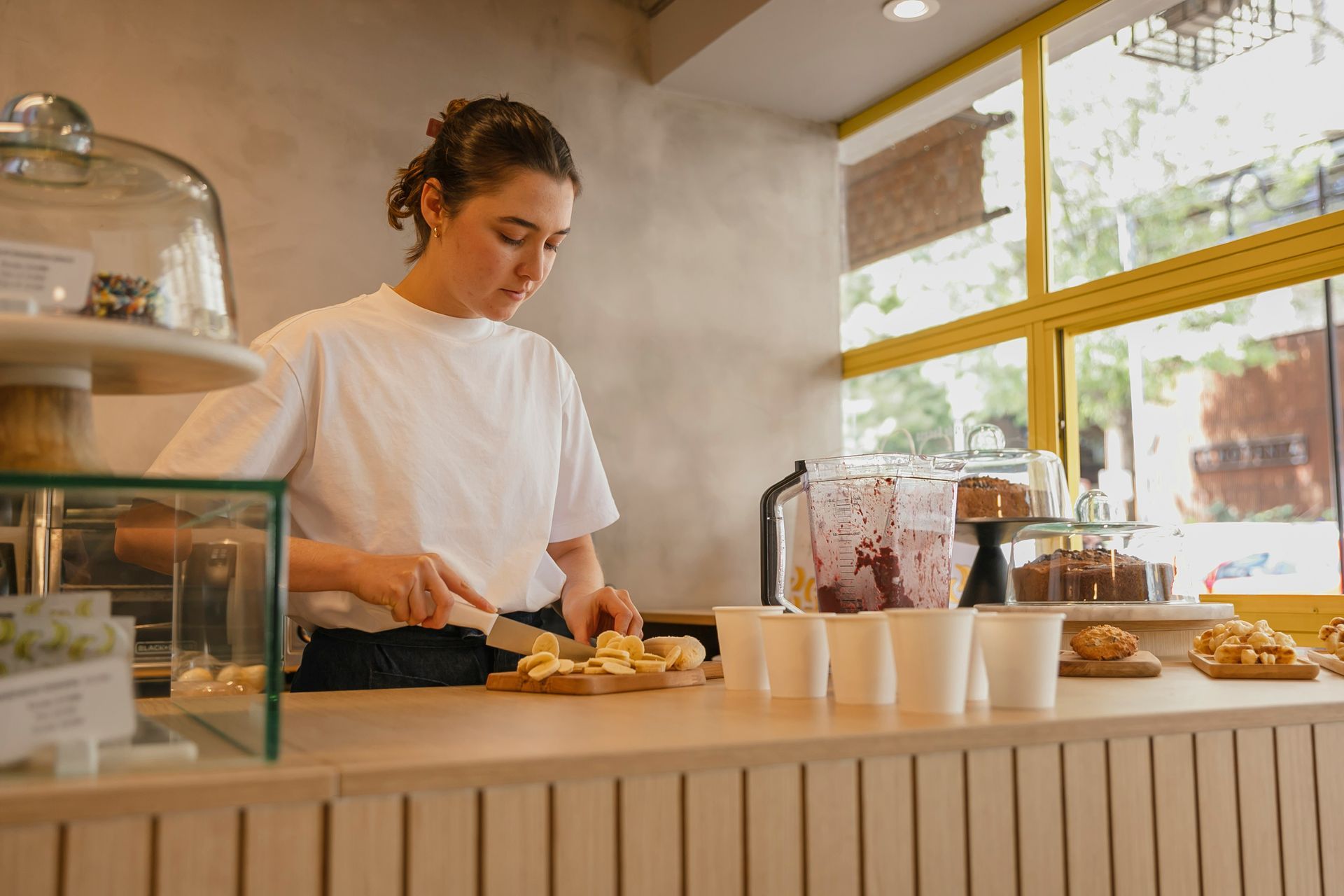 Barista preparing pastries at a café counter by a bright window