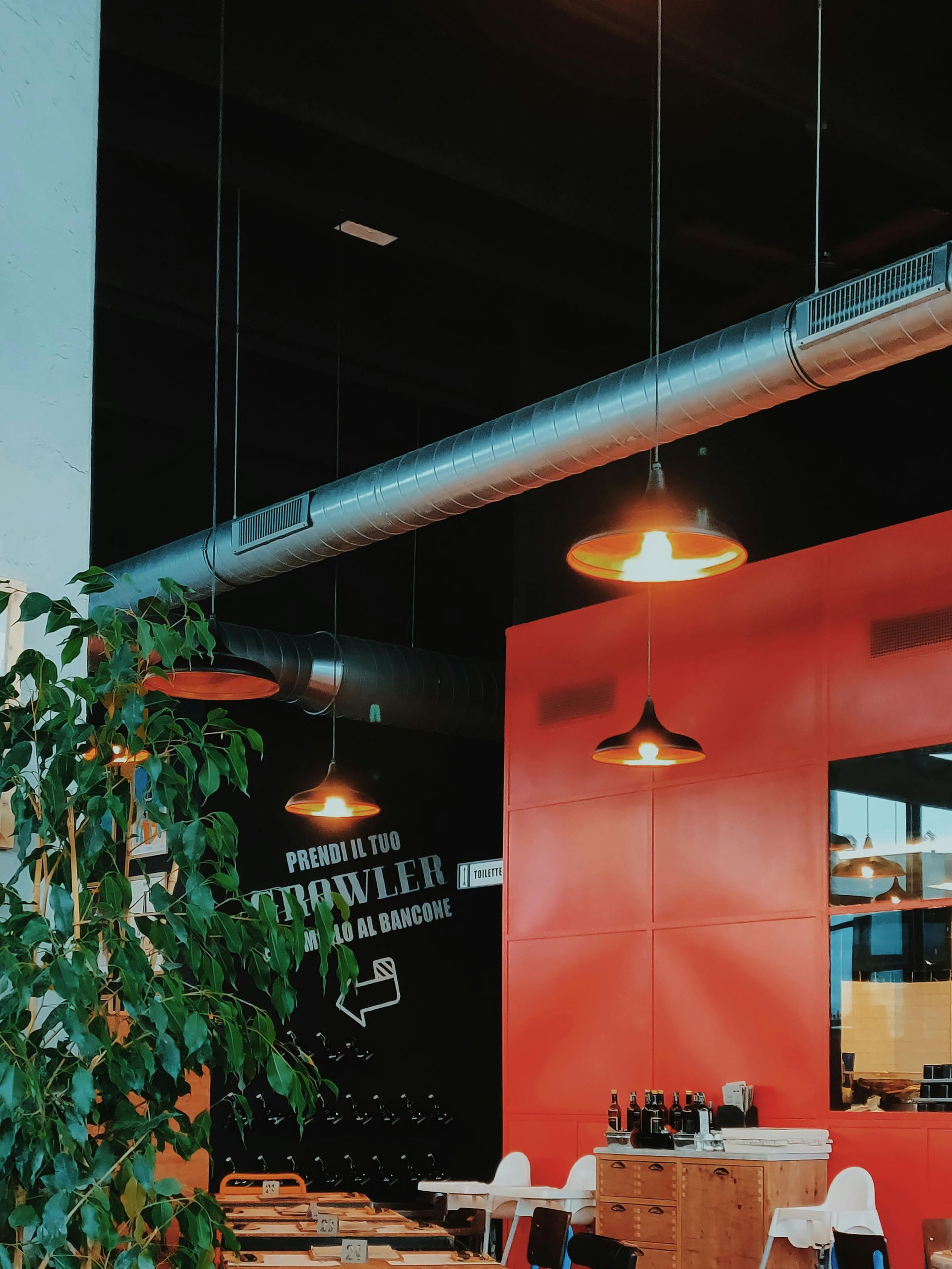 Modern cafe interior with red walls, hanging lamps, plants, and a table set for dining