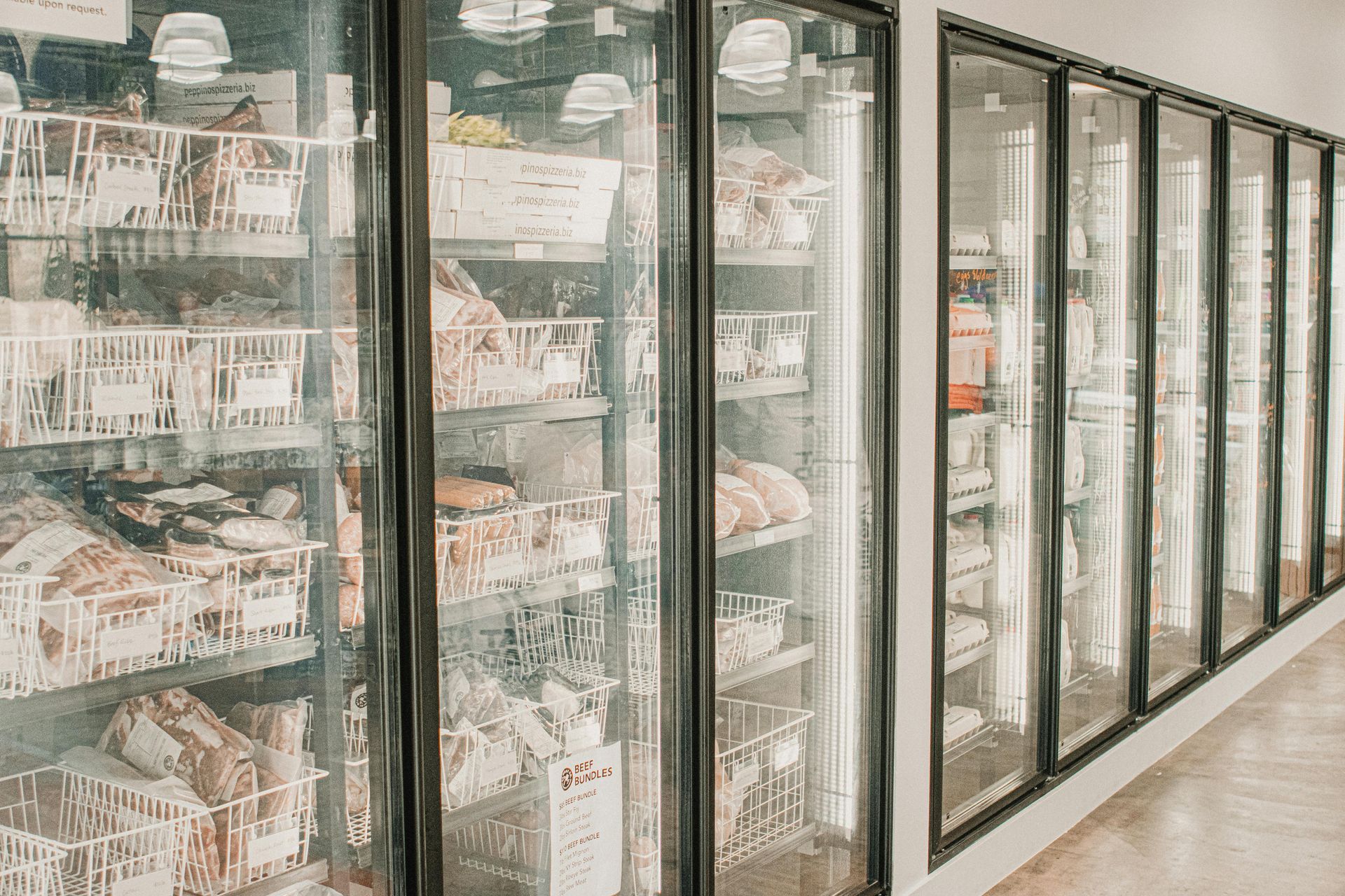 Row of glass-door freezer cases stocked with packaged food in a bright grocery store aisle