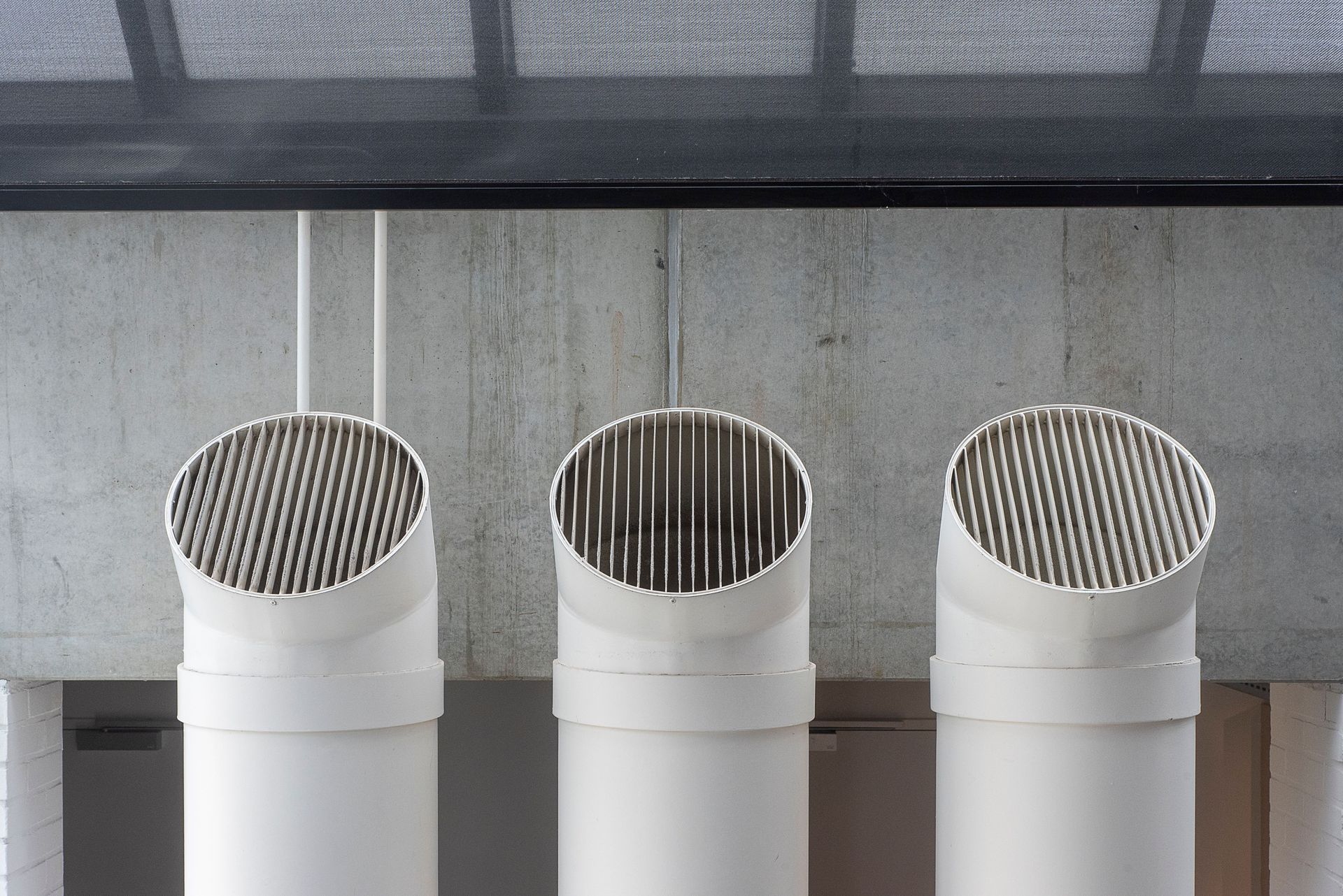 Three white vent pipes with striped metal caps against a gray concrete wall.