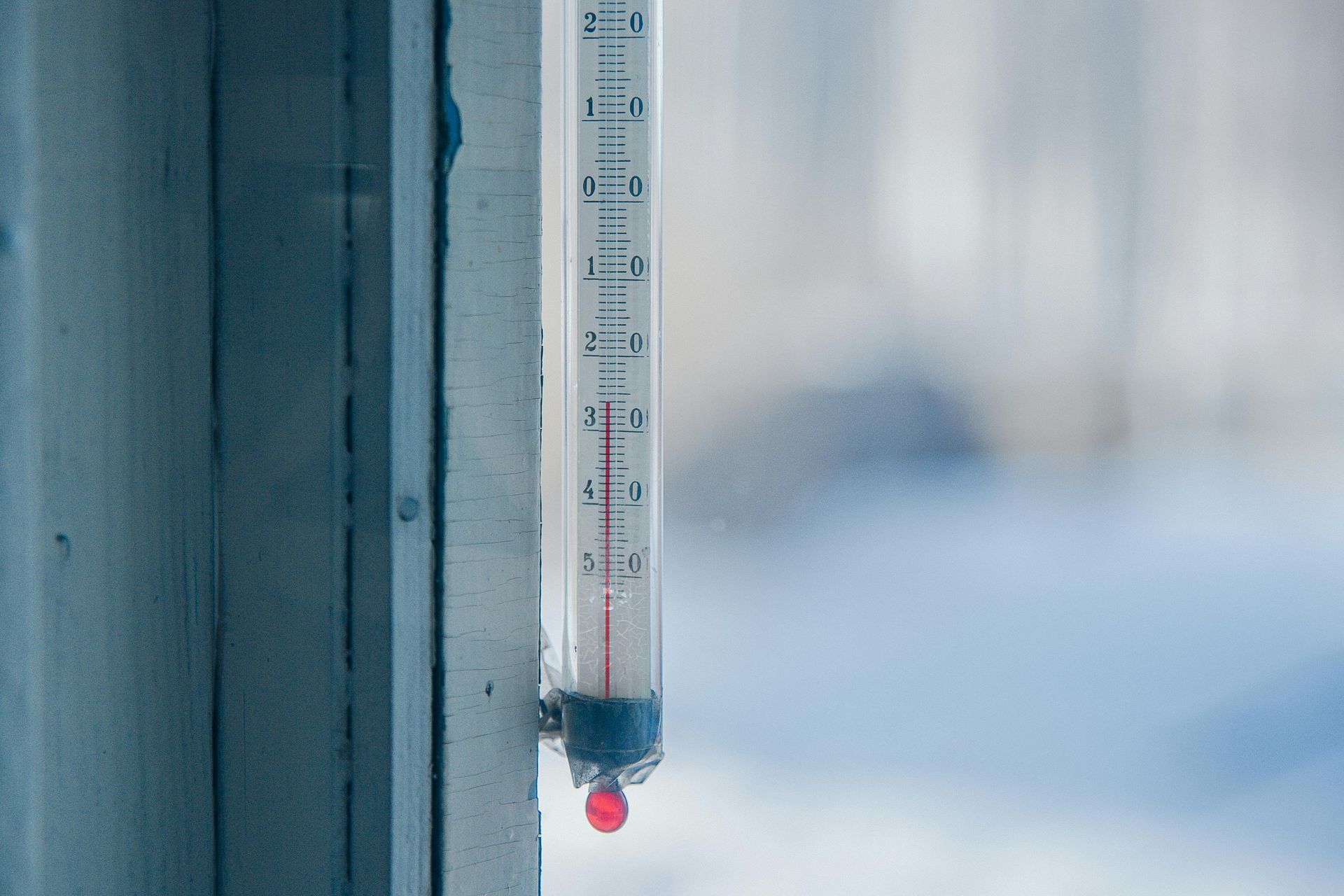 Outdoor thermometer hanging by a window, showing a cold temperature with snow in the background