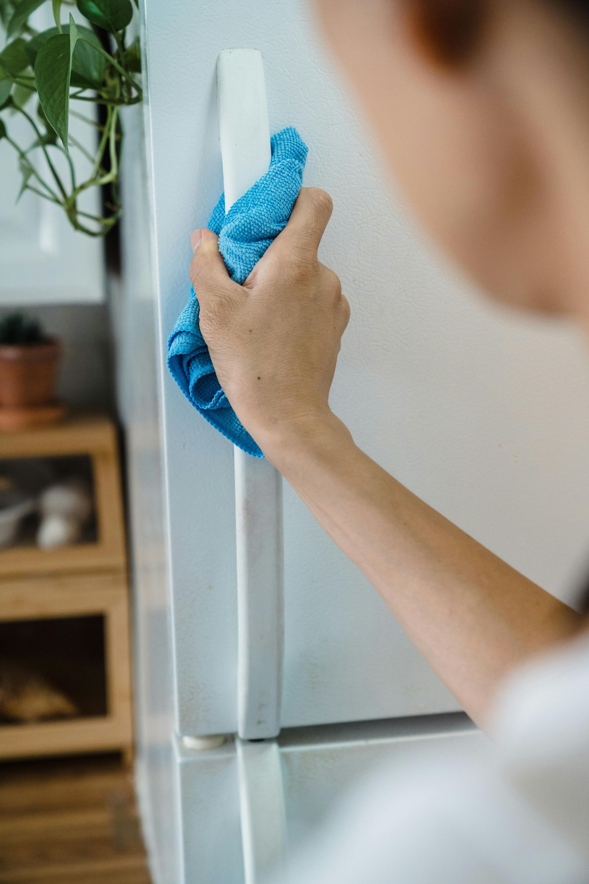 Hand wiping the side of a stainless steel refrigerator with a blue cloth.