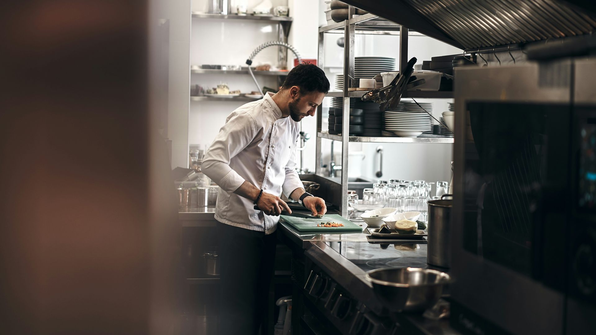 Chef plating food in a stainless-steel restaurant kitchen under bright overhead lights
