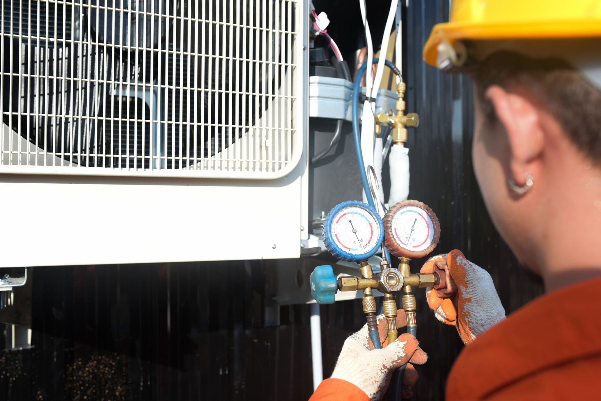 Technician checking gauges on HVAC unit beside a white fan grille