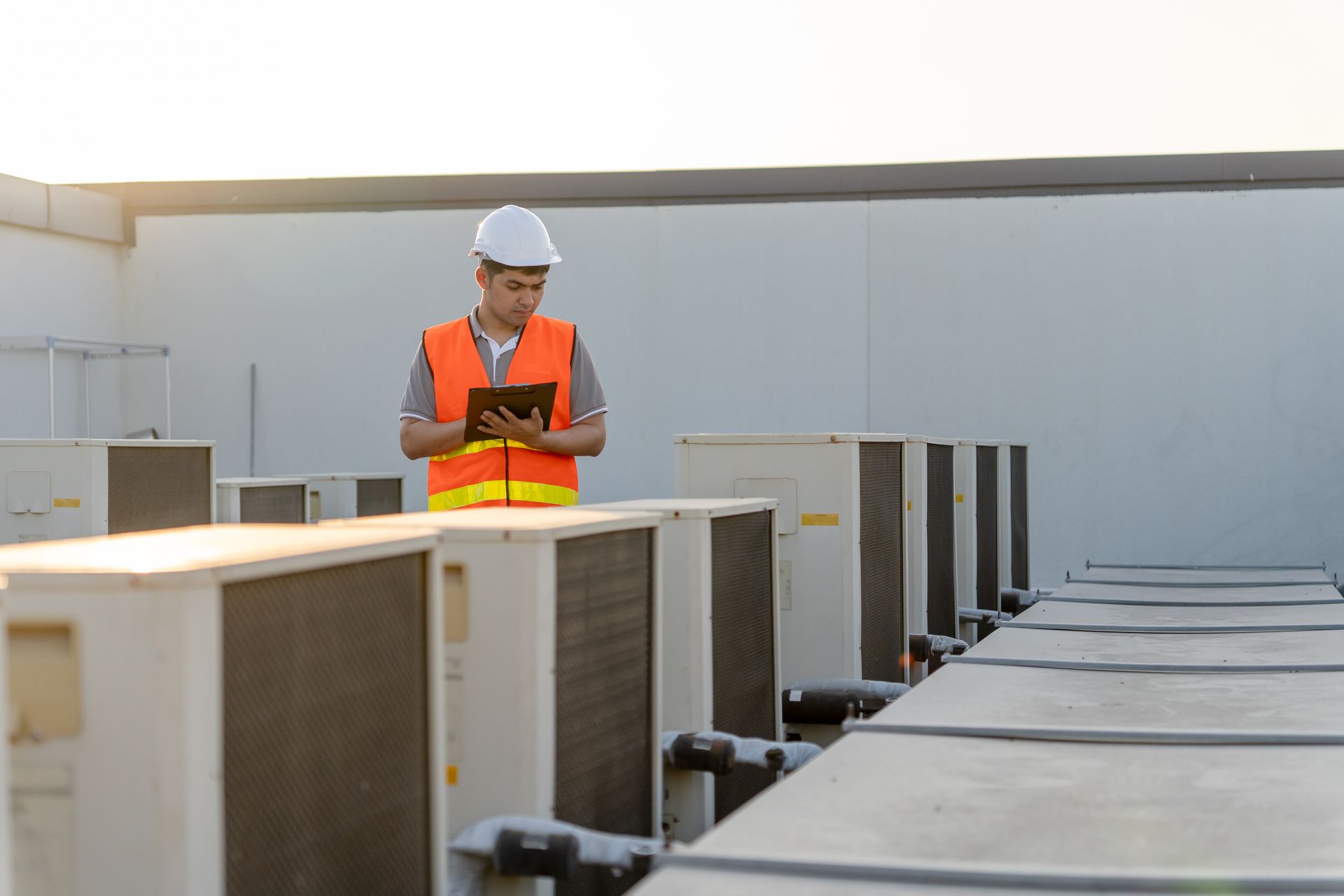 Technician in orange safety vest and hard hat inspecting rooftop HVAC units at a commercial building
