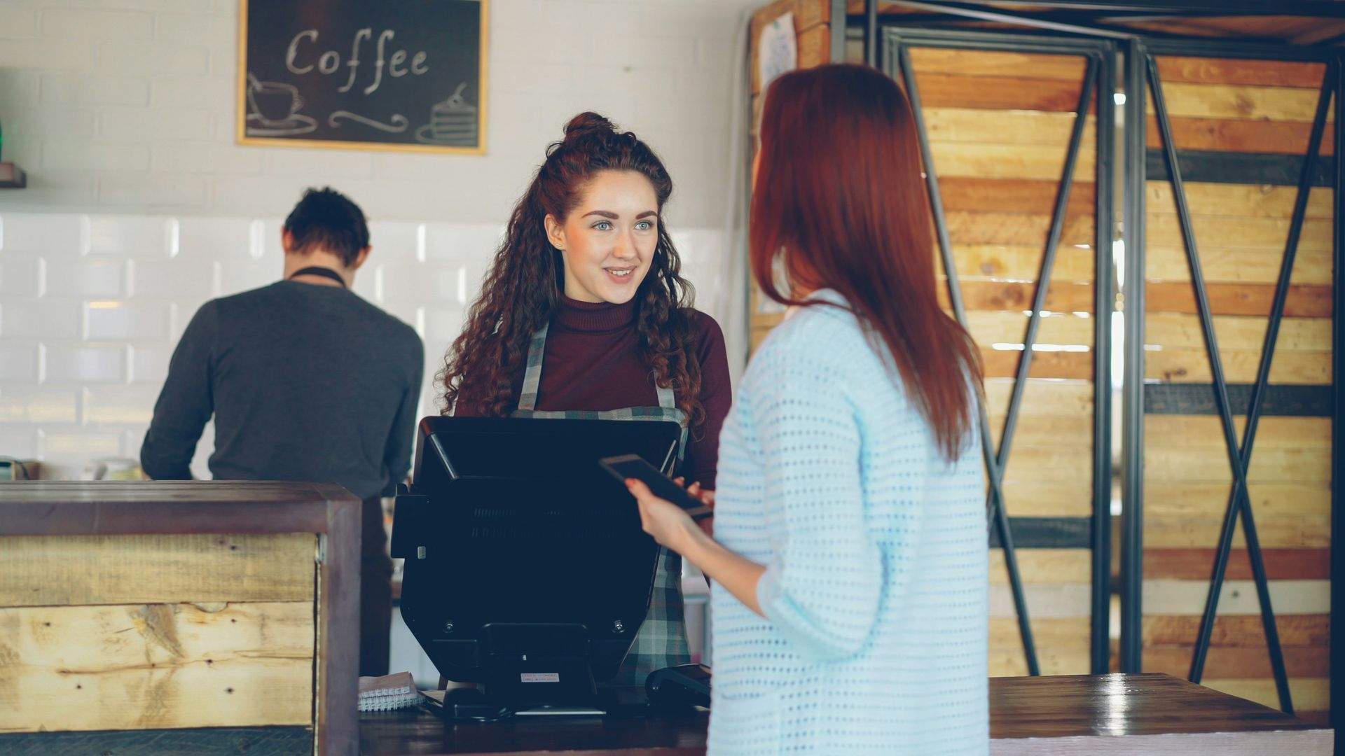 Barista taking an order from a customer at a café counter, with another customer in the background