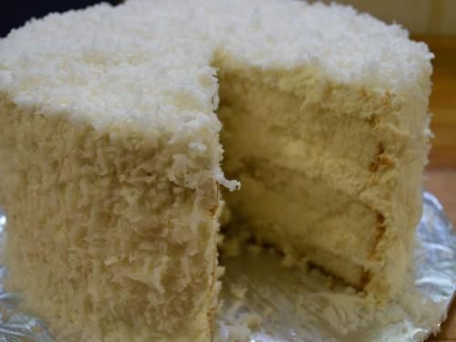 Coconut cake with a slice removed, showing layers of cake and frosting covered in shredded coconut.