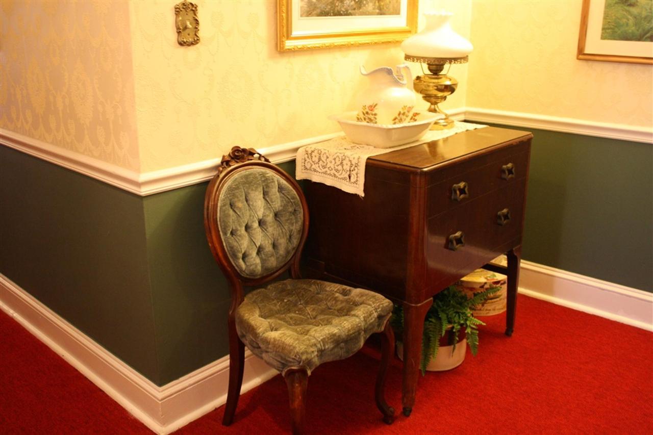 Antique chair next to a dark wooden chest in a corner with green and cream walls, red carpet, and a lamp.