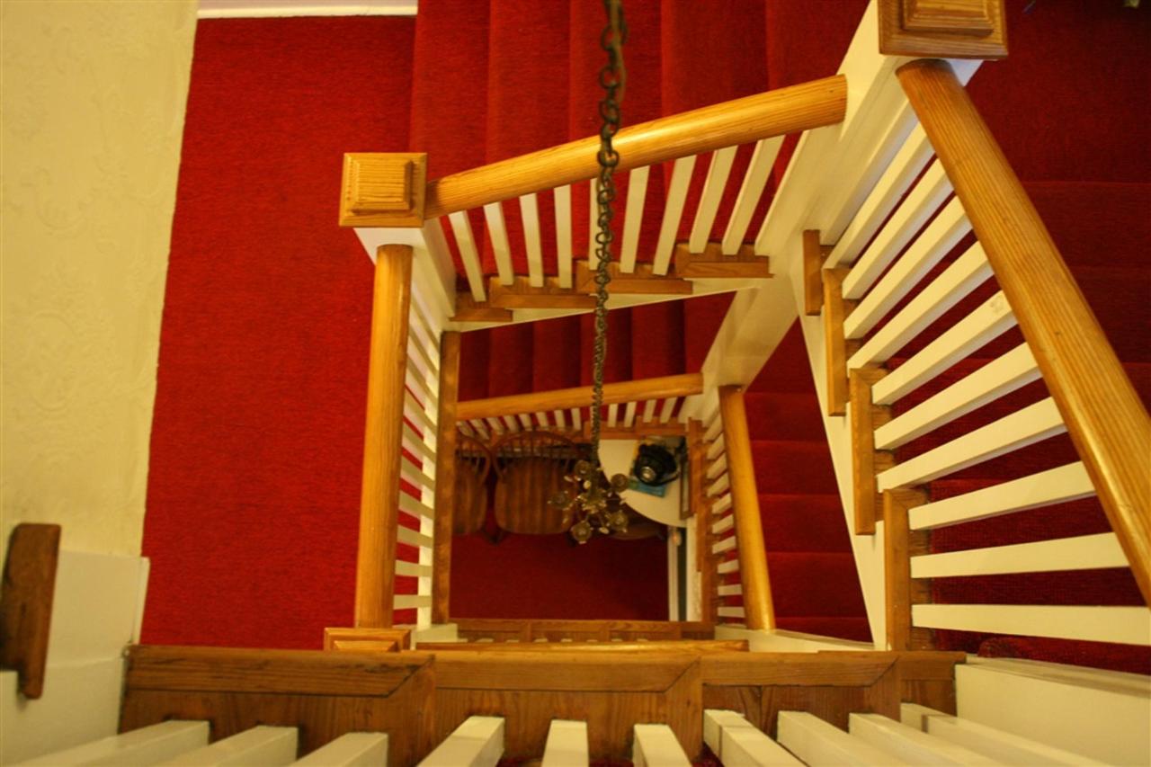 Top-down view of a red-carpeted staircase with wooden banisters. A light fixture hangs in the center.