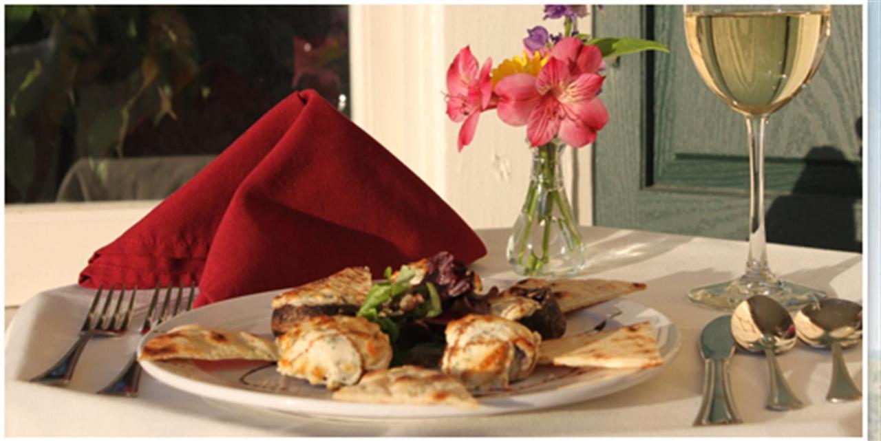 A plate of food, wine glass, and flowers on a table set for a meal; a red napkin is folded on the left.