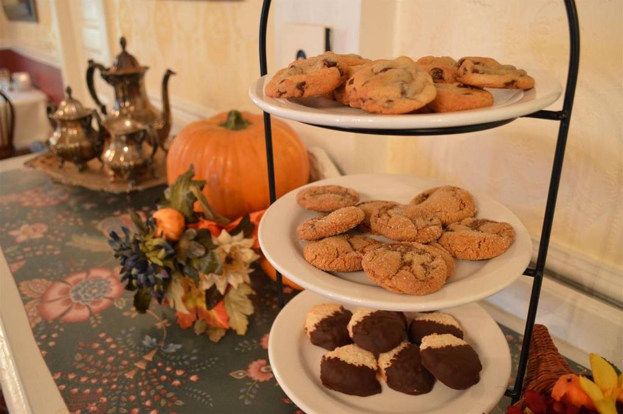Three-tiered serving tray with cookies, a pumpkin, and floral arrangement on a table in a cozy room.