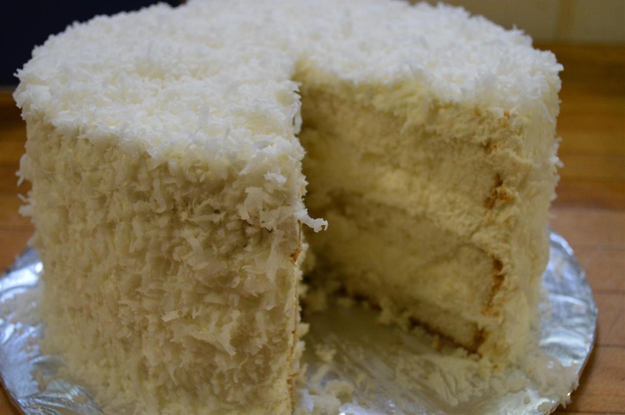 Coconut cake with a slice removed, showing layers and shredded coconut frosting.