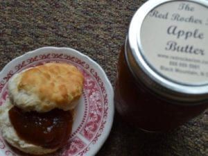 A jar of apple butter beside a biscuit topped with apple butter on a small, floral plate.