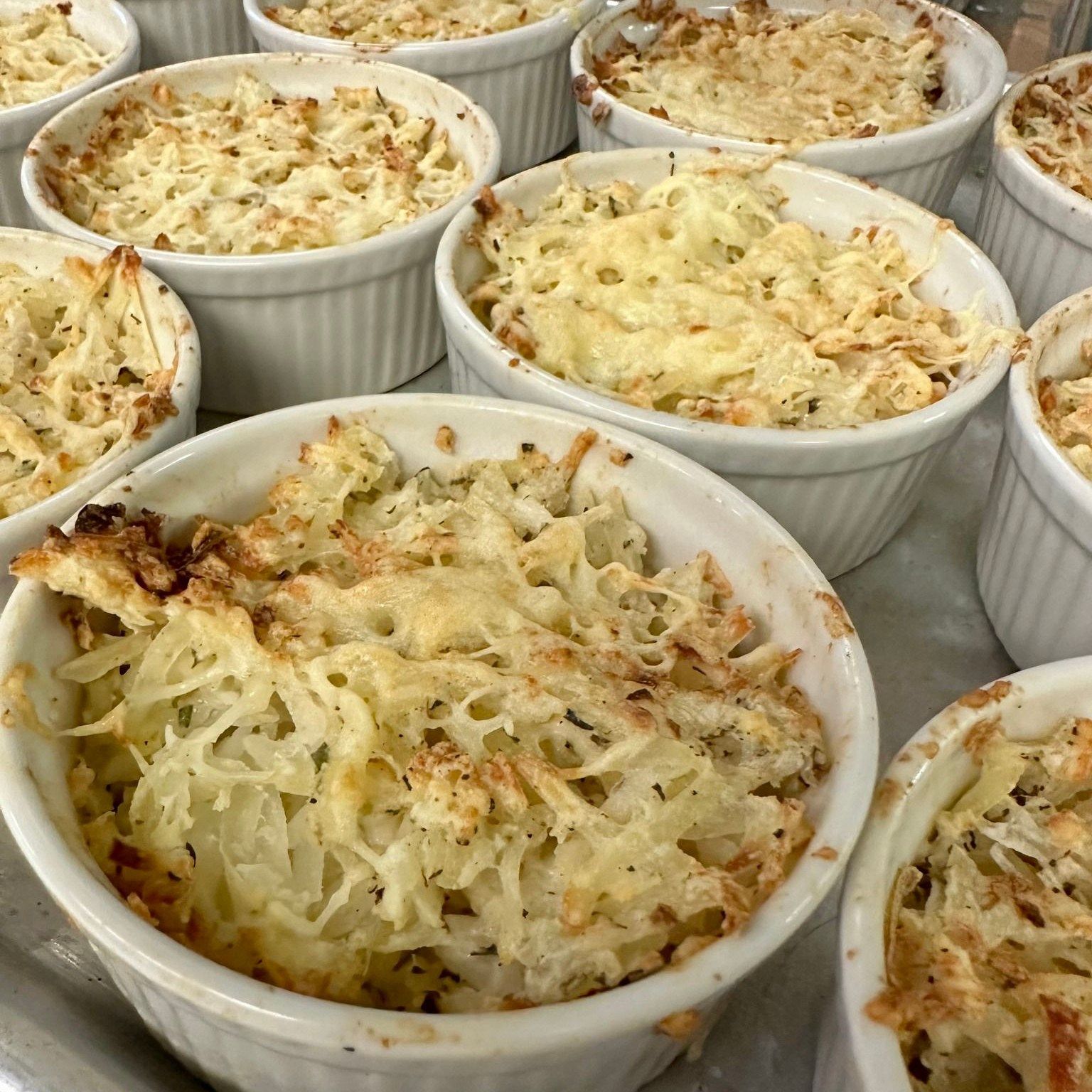 Close-up of several individual servings of potato gratin in white ramekins on a tray. The tops are golden brown and bubbly.