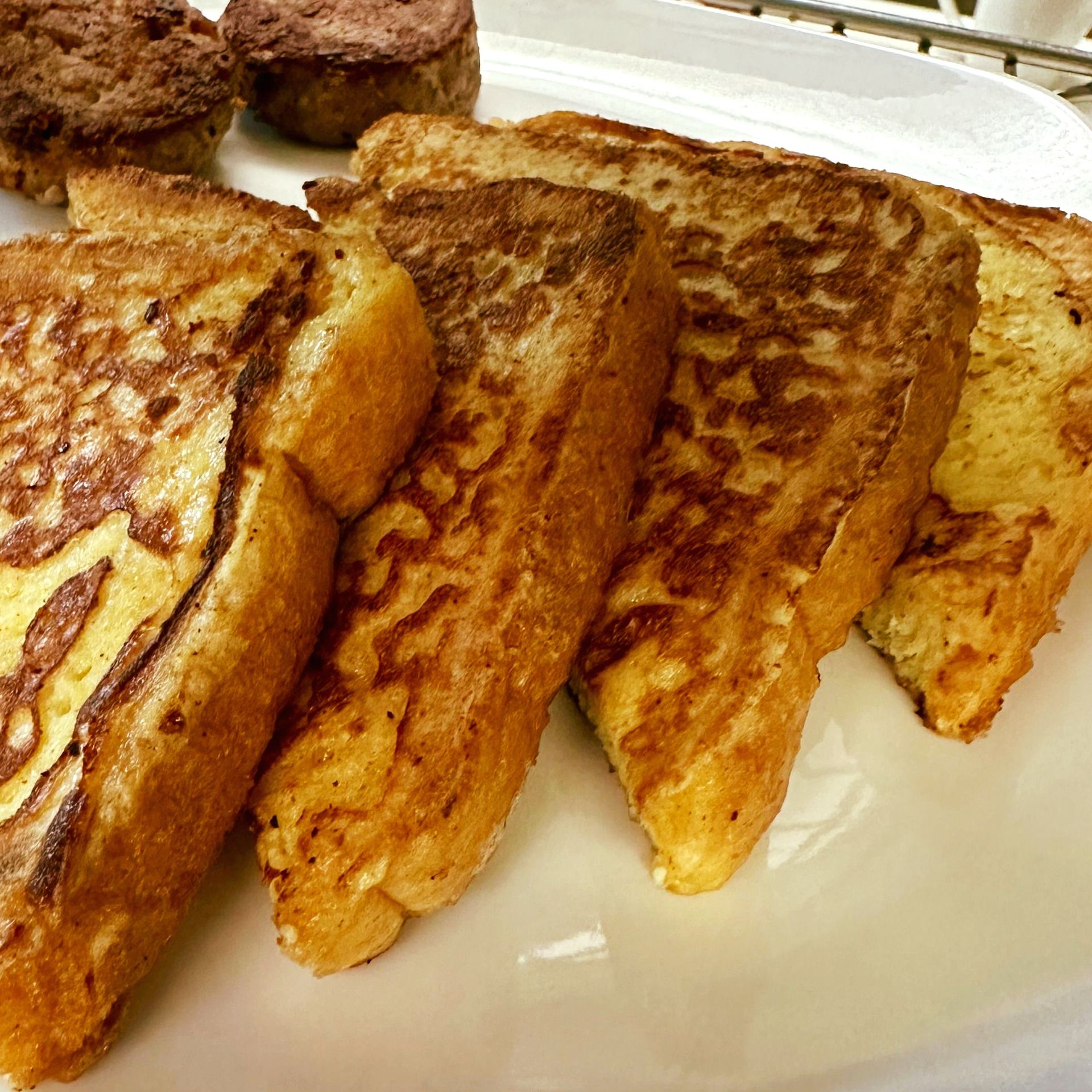 Golden-brown french toast slices with two sausage patties on a white plate, offering a delicious breakfast.