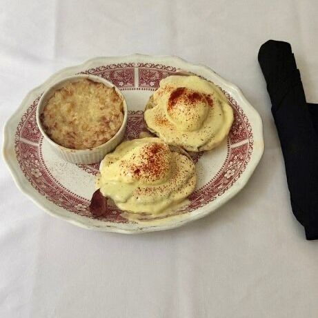Eggs Benedict with a side of gratin on a floral plate, alongside a rolled-up black napkin.