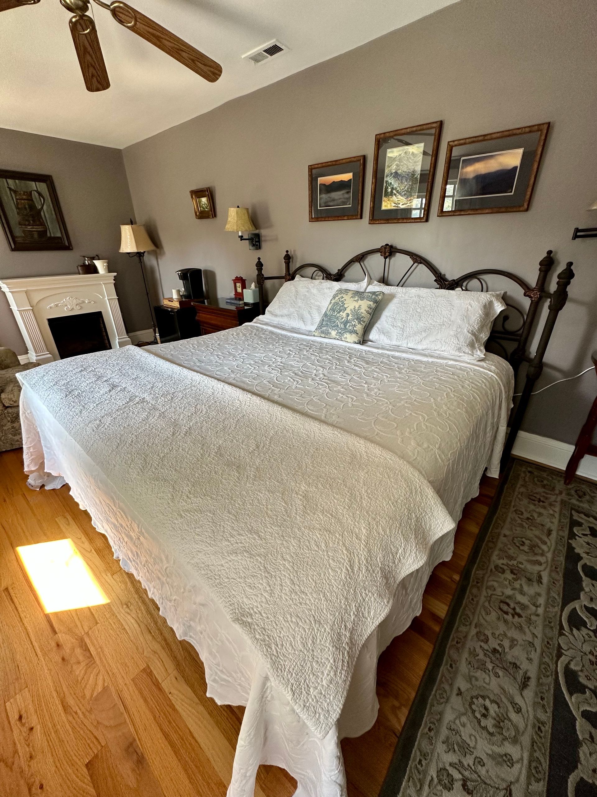 Bedroom with a bed covered in a white textured coverlet, wooden floor, gray walls, and framed art above the bed.