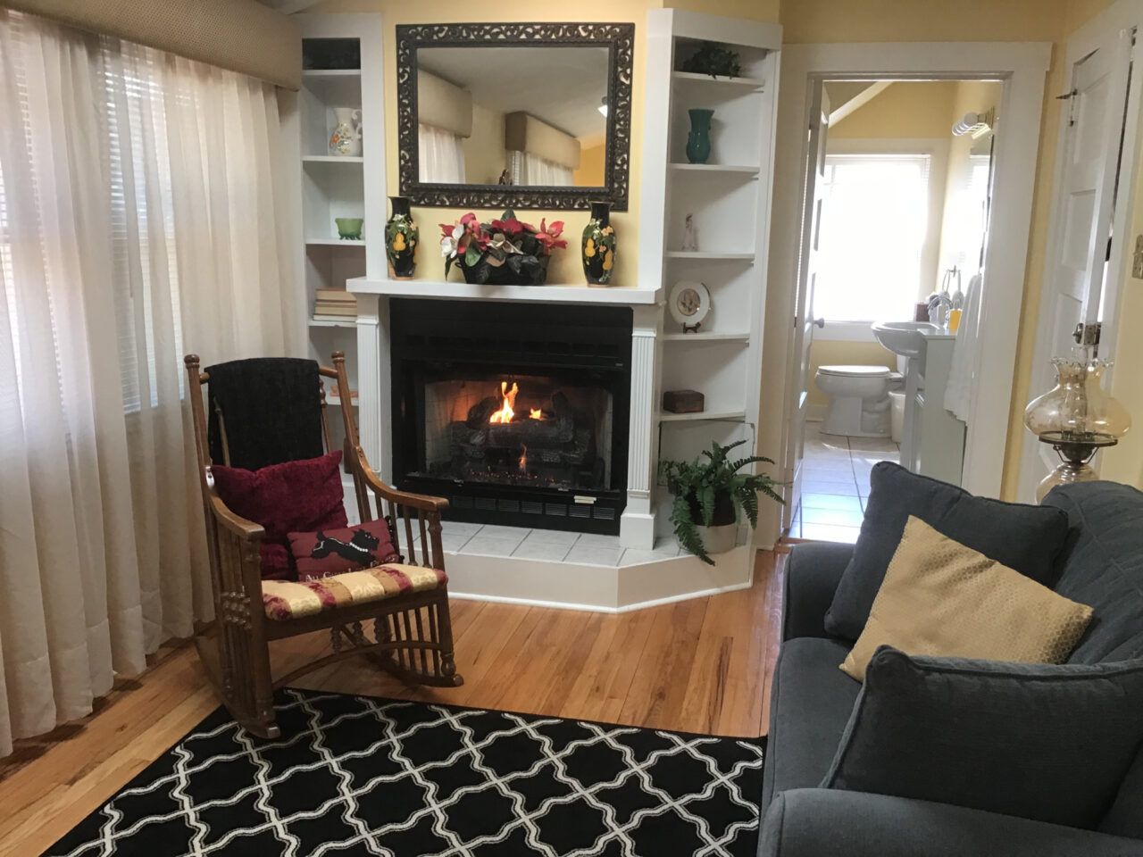 Cozy living room with fireplace, shelves, rocking chair, sofa, and a doorway to another room.