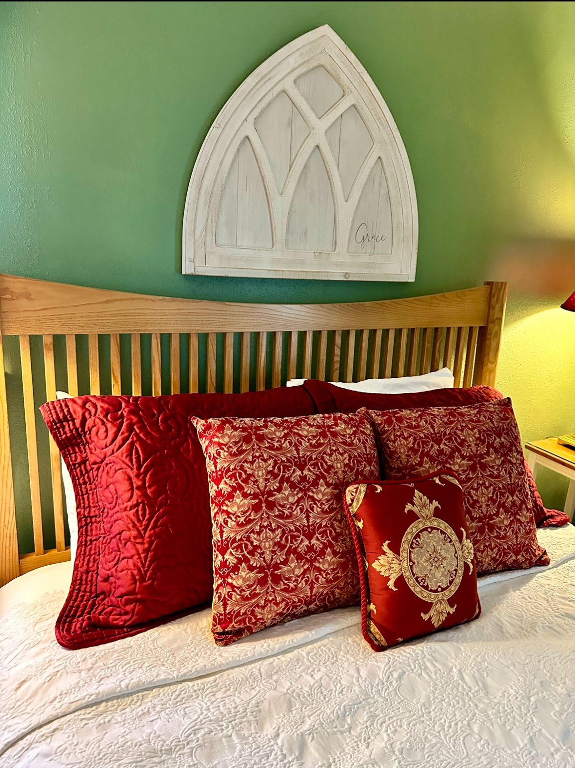 Bedroom with red pillows and a wooden headboard, green wall with white arched window decor.