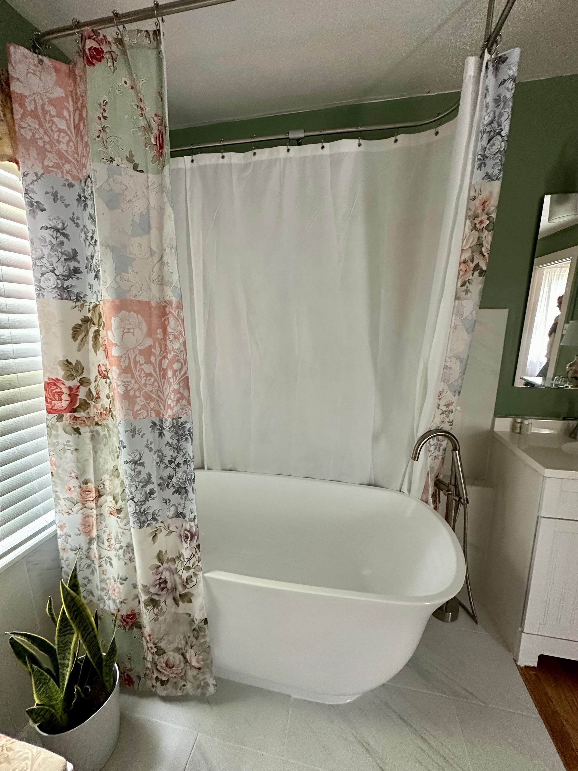 Clawfoot bathtub in a bathroom with floral patterned shower curtains and a window with blinds.