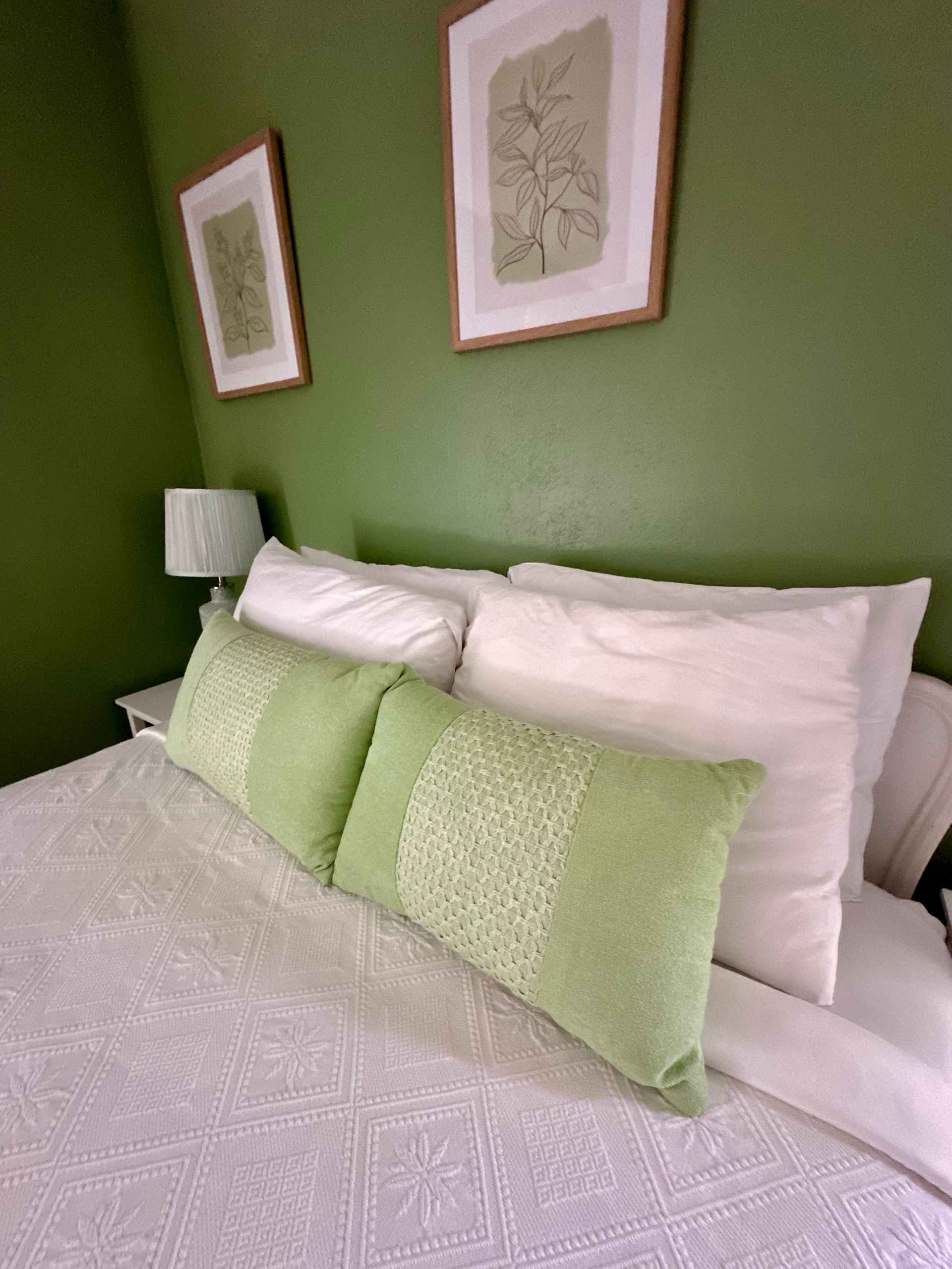 Green bedroom with white bedding and pillows, two green accent pillows, and framed art on the wall.