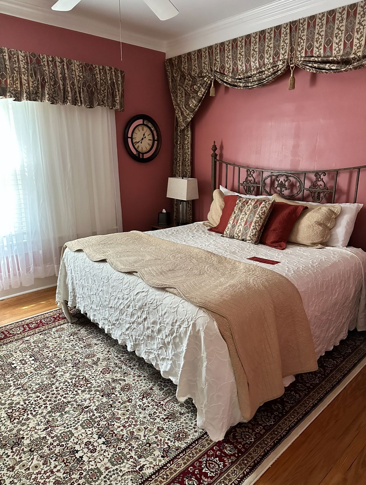 Bedroom with a bed, ornate headboard, red walls, patterned rug, and decorative window treatments.