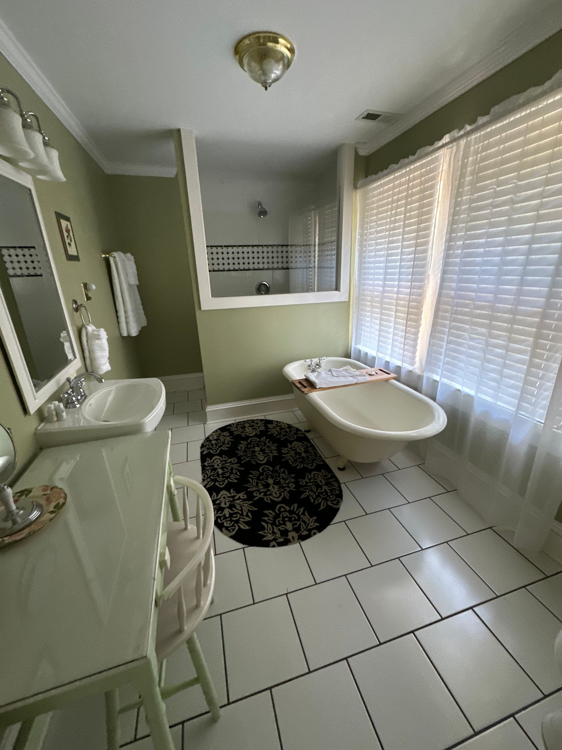 A vintage-style bathroom with a clawfoot tub and a small chair with a towel, light green walls.