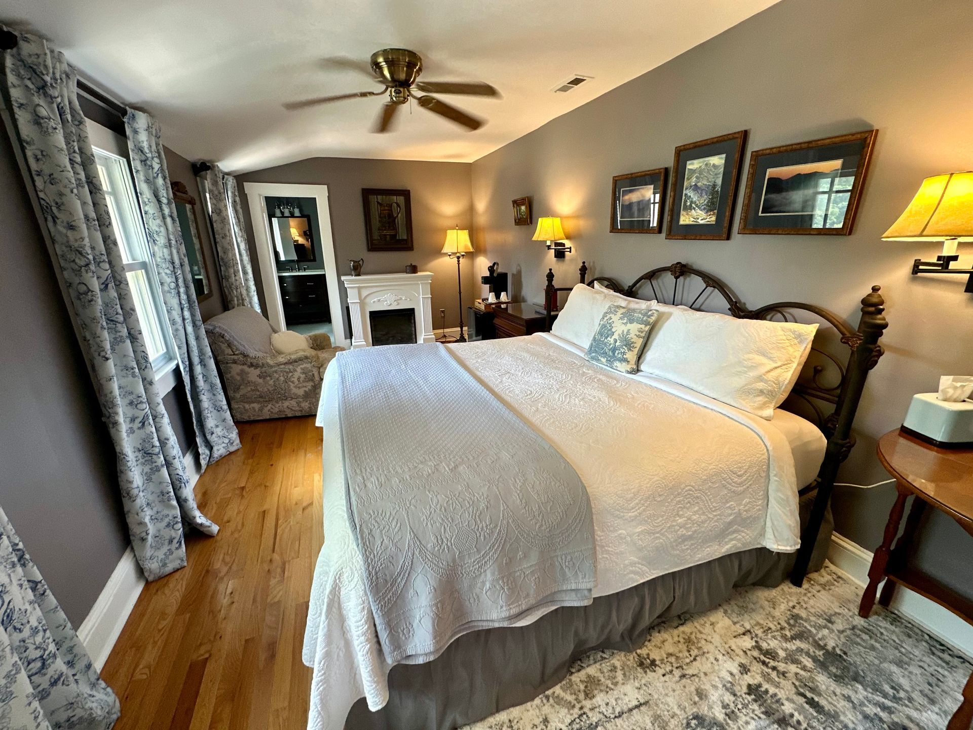 Bedroom with a bed, ornate headboard, and framed art. The room has hardwood floors and a gray color scheme.
