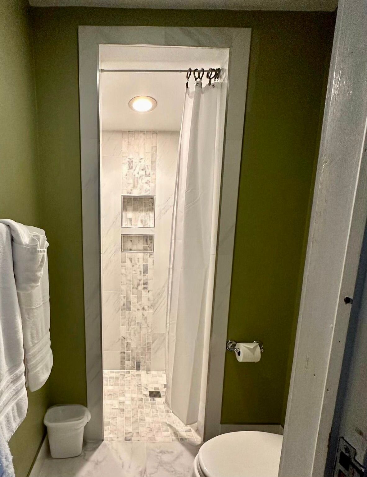Bathroom with a white shower curtain partially covering a shower. Green walls, white towels, and a toilet are also visible.
