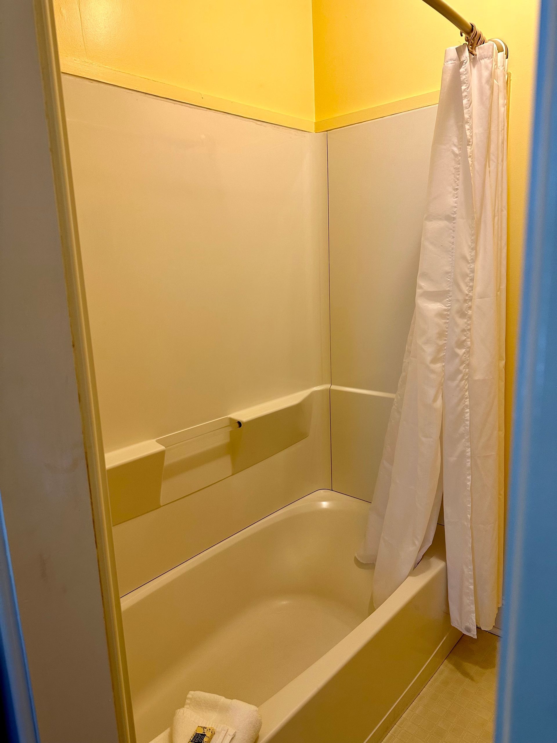 A small, off-white bathroom with a shower/tub combo and a partially closed white shower curtain; walls are yellow.