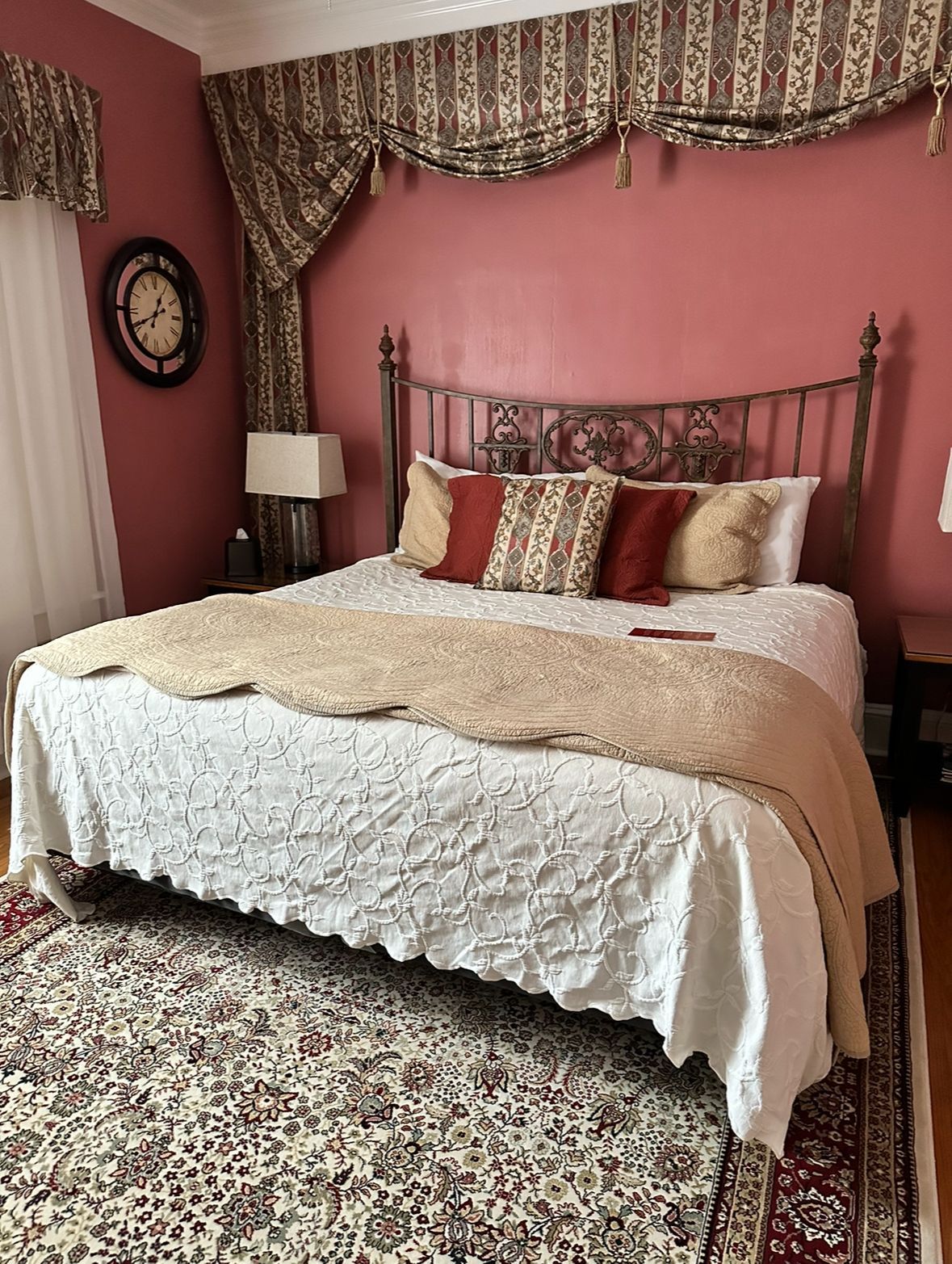 Bedroom with wrought iron bed, floral rug, and patterned valance, featuring red walls and decorative pillows.