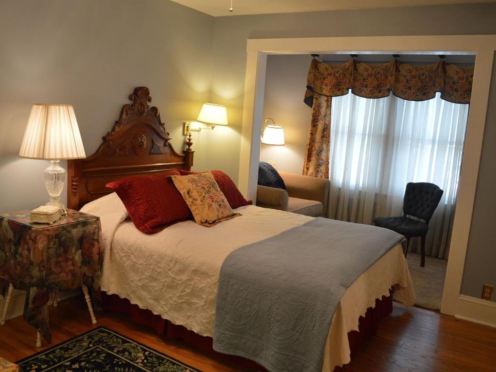 Bedroom with a bed, nightstand, and a doorway leading to a small seating area with a couch and window.