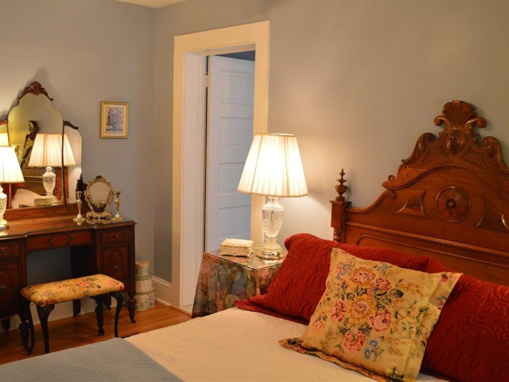 Bedroom with antique wooden furniture, including a vanity and bed. Red pillows and a floral pillow are on the bed.