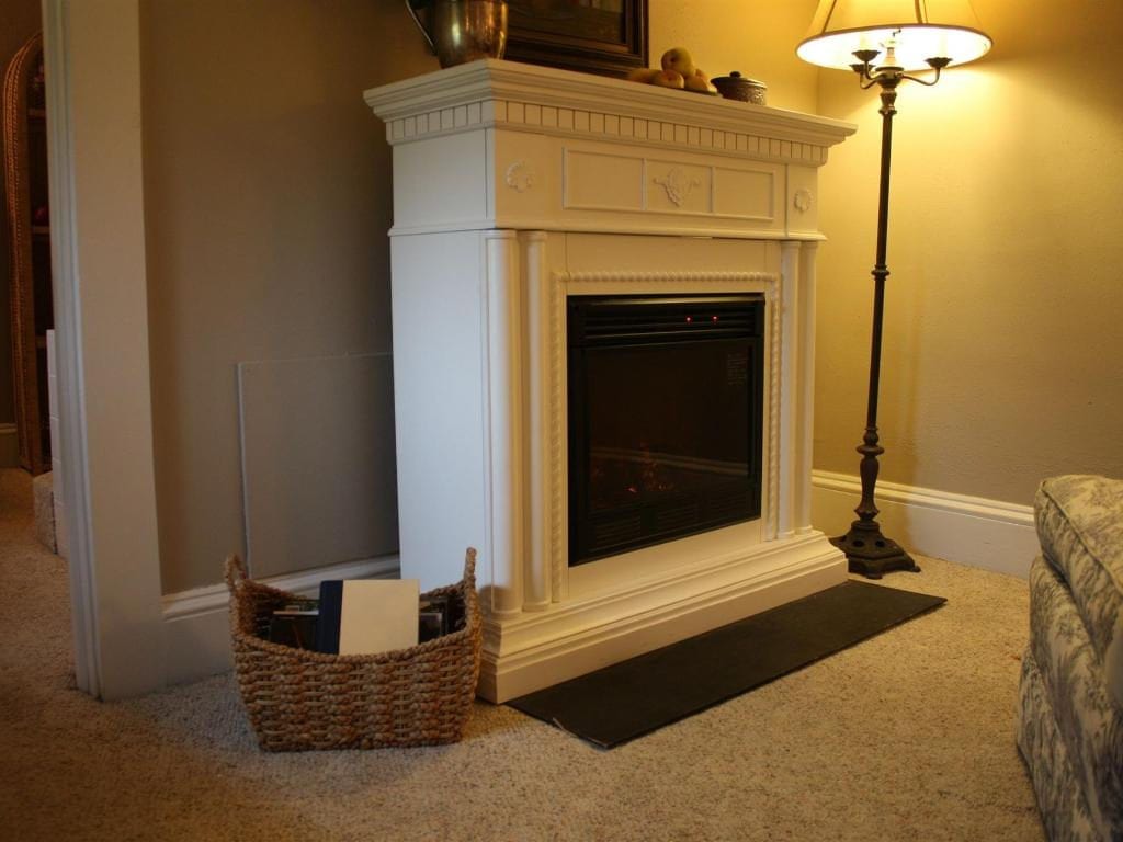 A white electric fireplace in a living room setting, with a basket, lamp, and rug nearby.