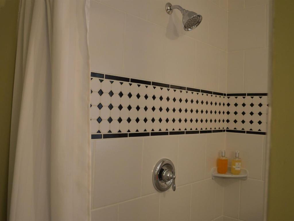 A white-tiled shower with black diamond-patterned trim, chrome fixtures, and a partially visible shower curtain.