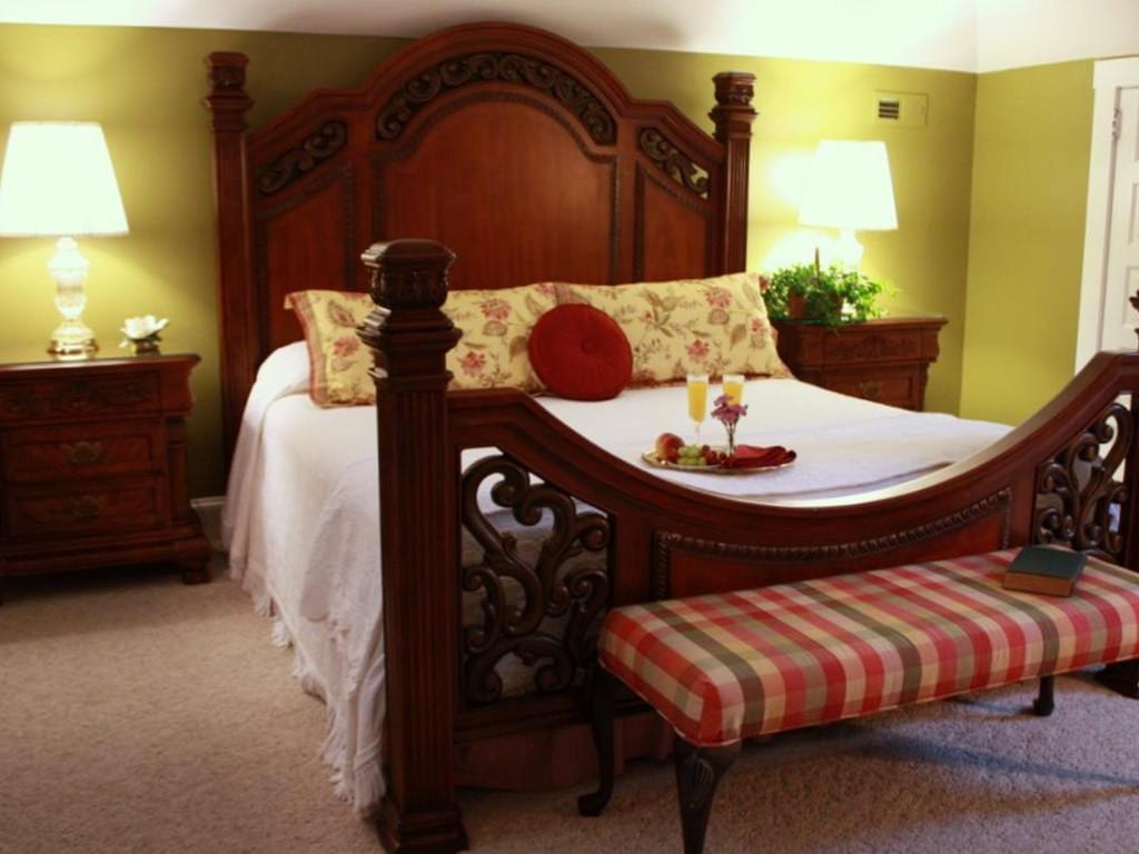 Elegant bedroom with a large wooden bed, nightstands, lamps, and a bench with a checkered cushion.