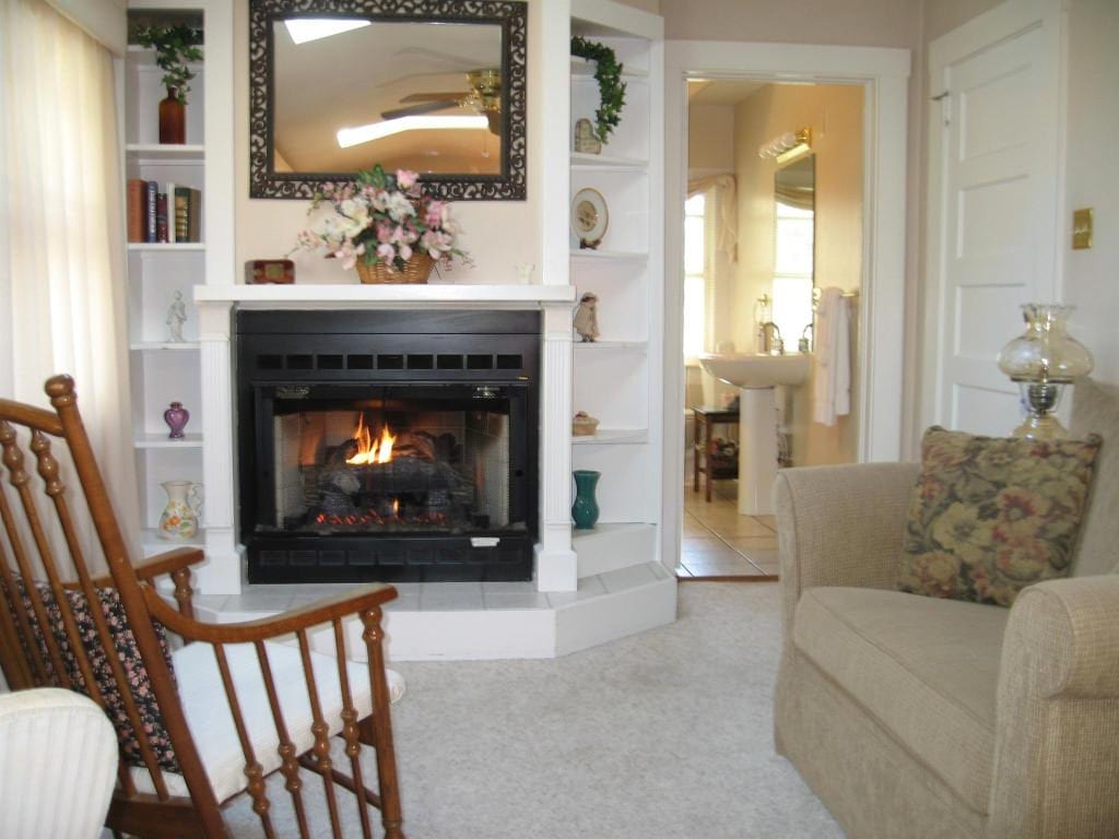 Cozy living room with a fireplace, bookshelves, rocking chair, and an open doorway to a bathroom.
