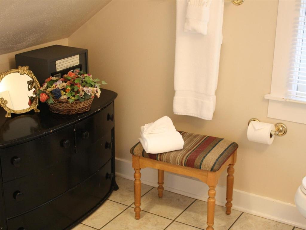 A bathroom with a black dresser, a bench with a towel, and hanging white towels.