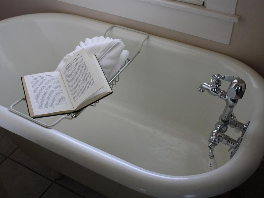 A white bathtub with a book on a rack, ready for a relaxing bath. Faucet running; a folded towel is present.
