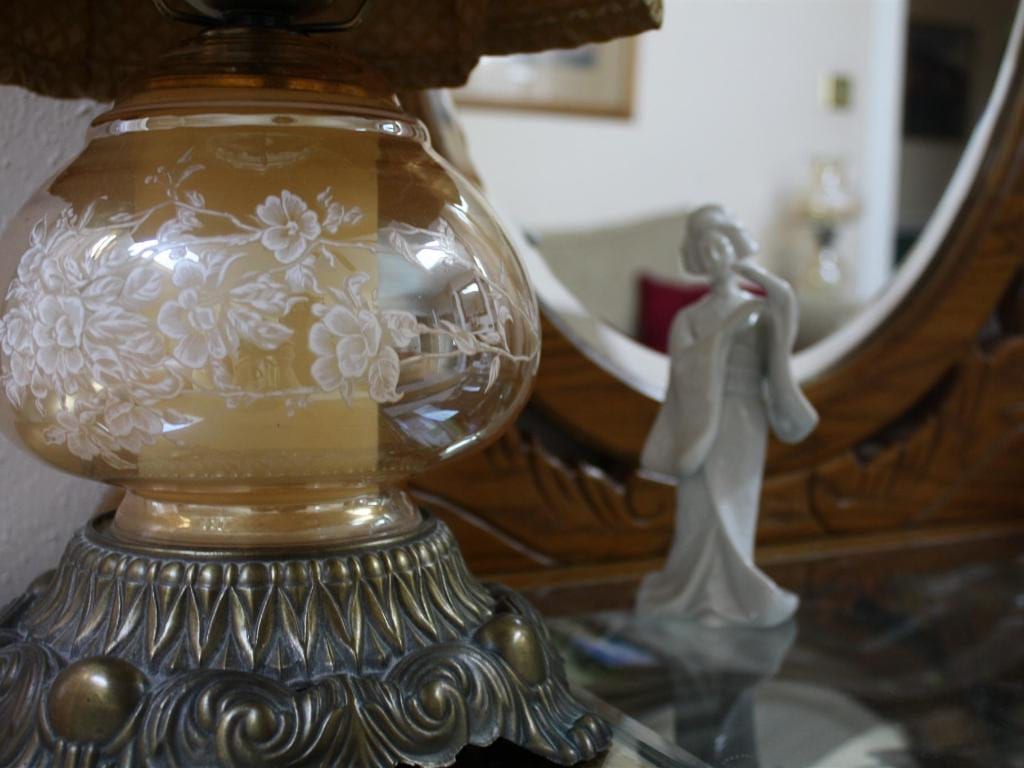 Close-up of a vintage lamp with floral etching, a white figurine, and a decorative mirror in the background.