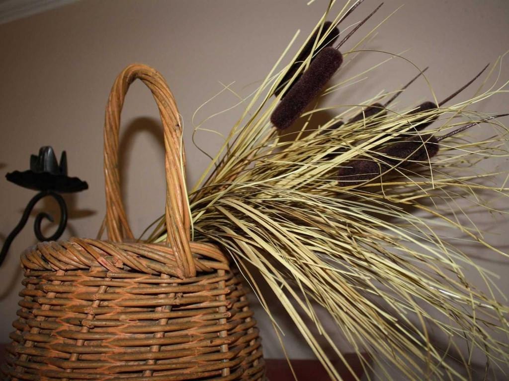 Wicker basket with tall dried grasses and cattails; a dark candle holder is visible on the left.